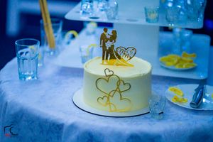 Wedding cake decorated with gold hearts and couple topper on blue-lit table.
