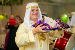 Performer in traditional Arabian dress holds a tray of treats at a festive celebration.
