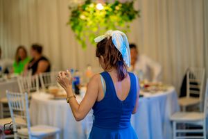 Guest in blue dress dancing at wedding reception with white decorated tables.