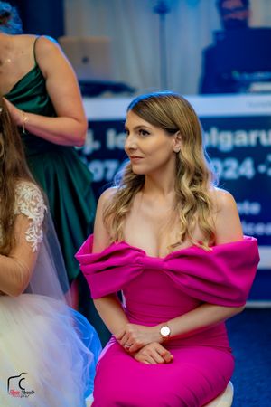 Wedding guest in vibrant pink off-shoulder formal dress at reception venue.
