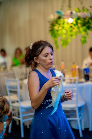Guest in royal blue formal dress at wedding reception with white table settings.