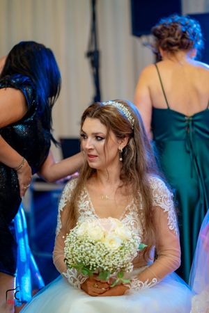 Bride in white lace gown with baby's breath bouquet surrounded by wedding party members.