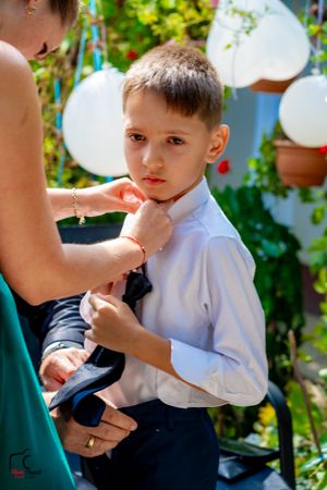 Child getting dressed in formal attire with help in outdoor garden setting.