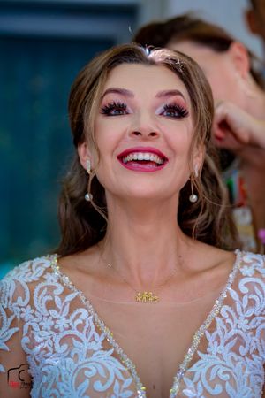 Wedding day portrait showcasing radiant smile, pink makeup and intricate white lace dress.