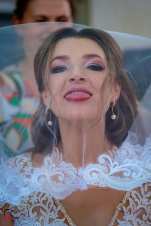 Bride wearing delicate lace wedding dress with pearl earrings and soft makeup.
