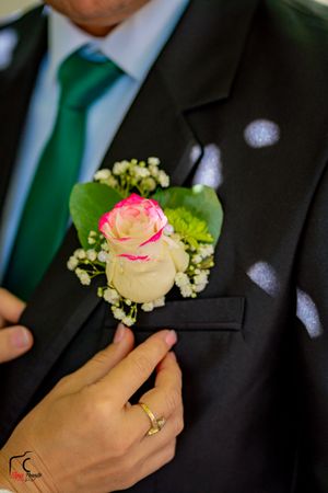 Close-up of hands pinning a pink and cream rose boutonniere onto a dark suit jacket.