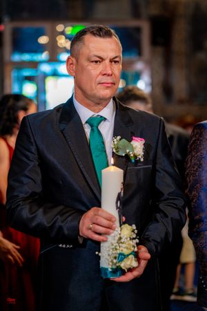 A guest in a dark suit and emerald green tie holds a decorated candle at a formal ceremony.