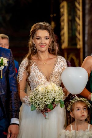 A bride in a white lace dress holds a bouquet of flowers with a white balloon nearby.