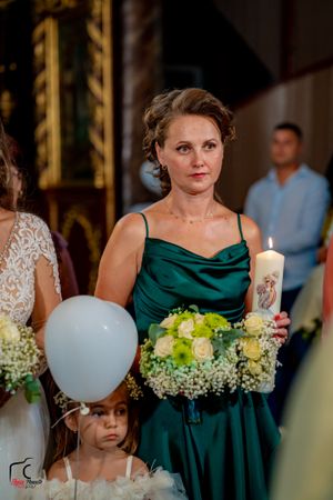 Wedding party members in emerald gowns holding bouquets and balloons.
