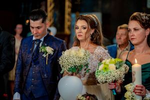 Wedding party members hold floral bouquets during an indoor ceremony.