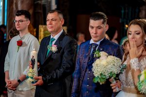 Wedding ceremony participants stand in formal attire with boutonnieres and flowers during the service.