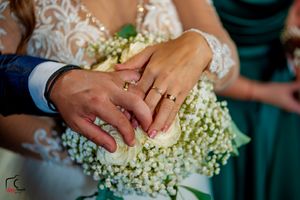 Hands displaying wedding rings over an elegant bridal bouquet of white roses and baby's breath.