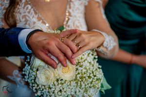 Close-up of wedding rings displayed on a white rose and baby's breath bouquet with hands showing the jewelry.