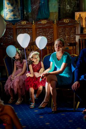 Group of guests sitting on ornate chairs with white balloons at an indoor venue.