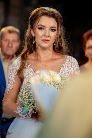 Person in white lace wedding dress holds bouquet during formal ceremony.