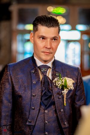 Person wearing blue patterned suit with boutonniere at formal event.