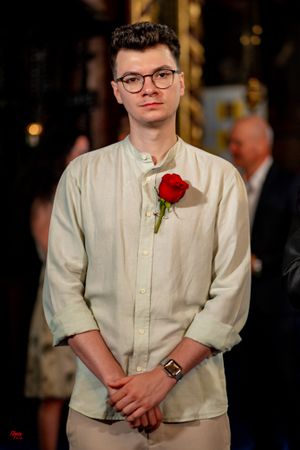 Guest in cream colored shirt with red rose boutonniere at formal event.