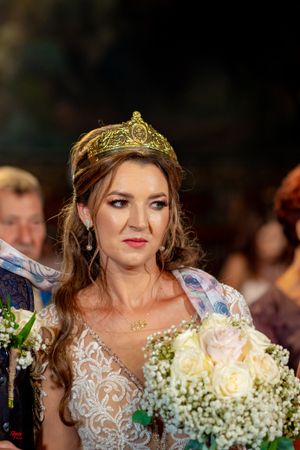 Close-up of bride wearing delicate golden tiara and holding white rose bouquet.