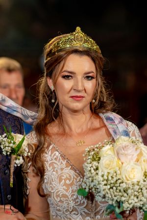 Bride wearing intricate lace dress and ornate golden crown with white floral bouquet.