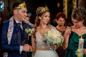 Wedding ceremony participants in elegant attire with golden crowns and lit candles.