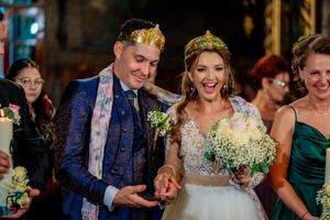 Newlyweds share excited moment during reception while wearing golden crowns.