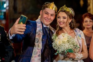 Couple takes celebratory selfie during wedding reception while wearing crowns.