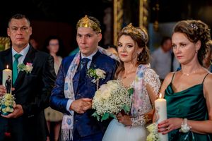 Wedding party in formal attire gathered during ceremony under ornate church chandeliers.