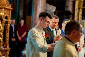 Wedding ceremony taking place in an ornate Orthodox church with gold decorations and chandeliers.