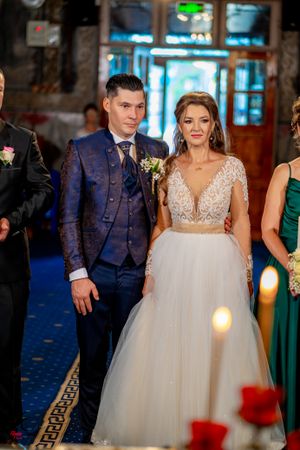 Bride in flowing white ballgown stands with wedding party members in a grand indoor venue.