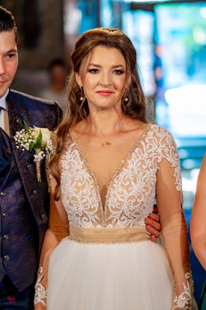 A wedding dress with intricate beaded lace overlay and sheer cap sleeves sparkles in indoor lighting.