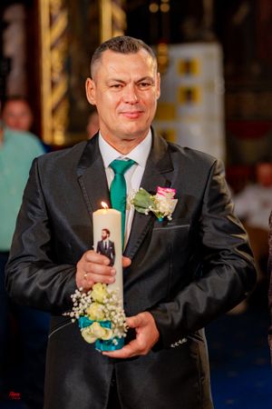 A wedding guest in a black suit and green tie holds a small floral boutonniere.