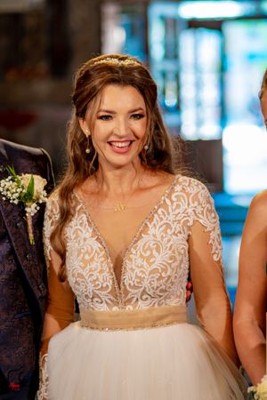 A bride in an elegant white lace wedding dress with beaded bodice and flowing tulle skirt smiles during her wedding celebration.