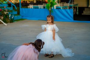 Two young flower girls in white and pink dresses playing at a wedding reception.