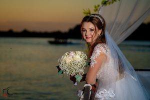 Wedding couple poses at sunset by the water under an elegant floral arch with white fabric.