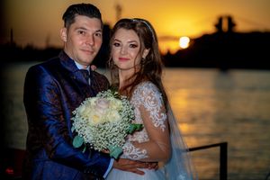 Newlyweds sharing intimate moment at sunset on boat deck with white floral bouquet.