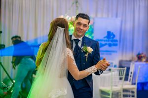 Wedding couple dances surrounded by atmospheric fog and colorful lighting effects at an indoor reception venue.