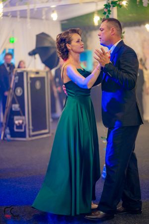 Couple dancing elegantly in formal attire with woman in green gown under blue lighting.