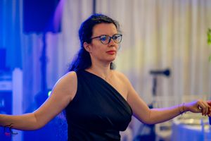 Dancer in elegant black one-shoulder dress performing at indoor celebration.