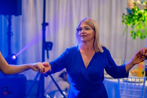 Dancer in royal blue wrap dress holding hands during group dance at indoor event.