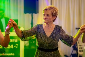Dancer in sparkly dress enjoying a festive moment under green and blue lighting.