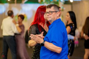 Couples dancing together at an indoor social event with colorful lighting and decorative elements.