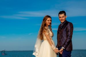 Wedding couple embraces on a wooden pier with the ocean and blue sky creating a stunning backdrop.