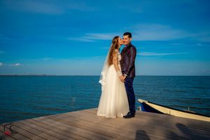 Wedding couple poses together on a wooden boardwalk against a beautiful ocean backdrop.