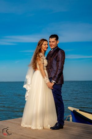 A romantic wedding photo session on a wooden pier overlooking a serene ocean under bright blue skies.