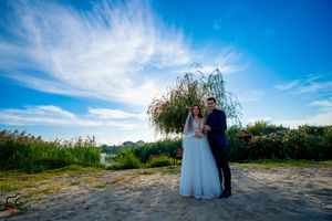 Panoramic wedding scene with couple amid natural landscape and dramatic sky.