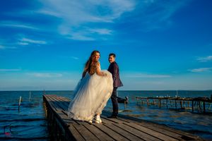 Wedding couple poses on a wooden pier extending into the ocean under clear blue skies.
