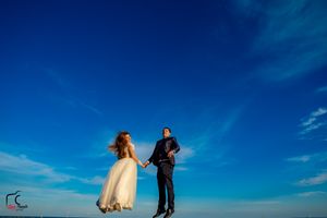 Artistic wedding shot on wooden pier with dramatic blue sky and ocean landscape.