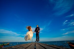 Seaside wedding moment captured on rustic pier against vibrant blue horizon.
