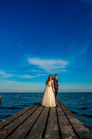 Scenic wedding photography on wooden boardwalk stretching into vast blue waters.