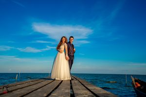 Elegant wedding scene on weathered pier with dramatic blue sky and ocean horizon.
